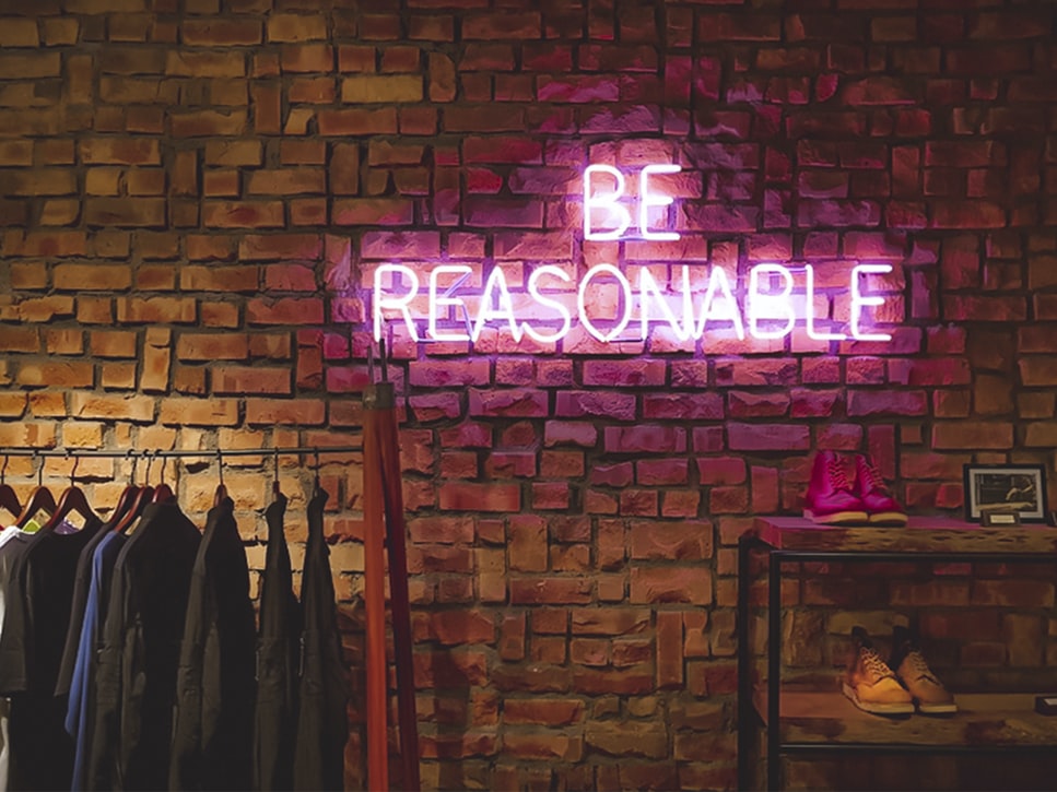 neon 'be reasonable' sign above a clothes rail